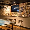 A TV on a wall with a ping pong table and bar stools in the foreground