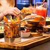 A burger served on a wooden board, with other dishes in the background