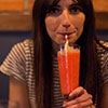 A woman drinking a red cocktail in a thin glass