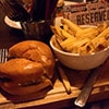 Close up of a burger and bowl of chips served on a wooden board