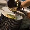 A chef pouring food onto a stack of plates from a pan