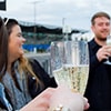 Close up of a pair of hands holding two champagne flutes with people stood in the background