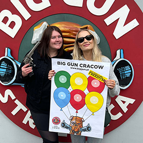 Two smiling females hold up a sign promoting a shooting range