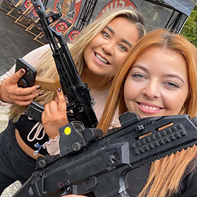 Two smiling females hold black guns 