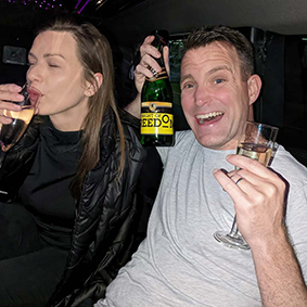 A smiling man holds a bottle of Champagne while sitting next to a female