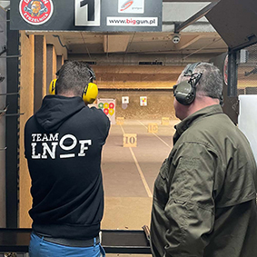 A male fires a gun at a shooting range while being supervised