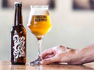 A bottle of craft beer with a hand holding a glass of beer