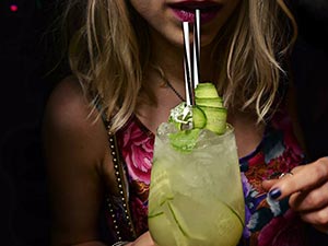 A girl drinking from two straws in a cucumber cocktail