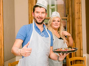 A man holding up his pizza with a woman in the background