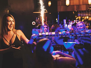 A woman carrying a round of shots with a sparkler coming out