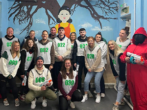 A group of people wearing Squid Games Bibs in front of a Squid Games Mural with a Guard from Squid Games in Newcastle