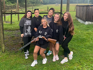 A group of women posing for the camera as one holds a shotgun. 
