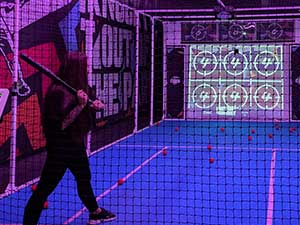 A woman holding a baseball bat about to play an arcade game 