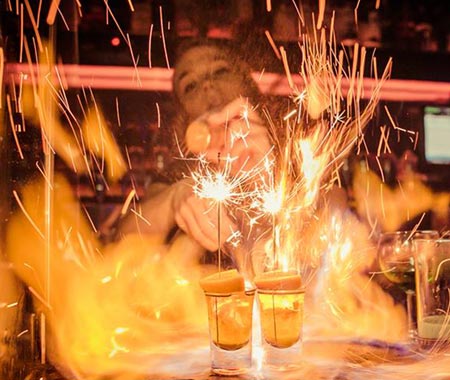A girl setting fire to two sparklers in some shots 