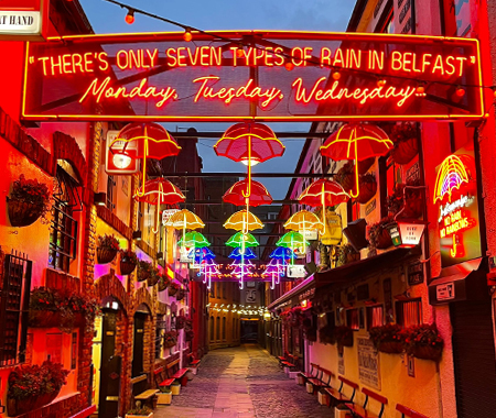 An umbrella-themed art instillation with neon umbrellas hanging from the sky in a street in Belfast. 
