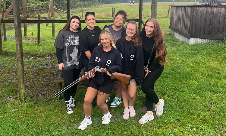 A group of women posing for the camera as one holds a shotgun. 