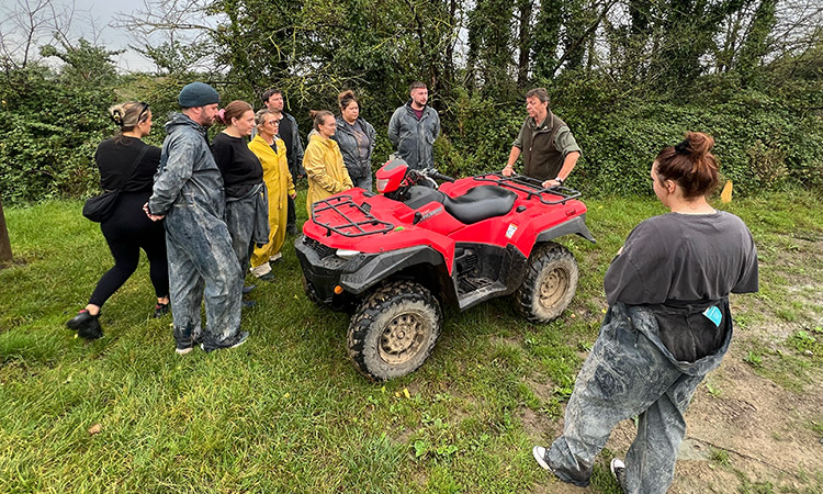 A group of people gathered around a quad bike as an instructor talks them through the health an safety of driving one. 