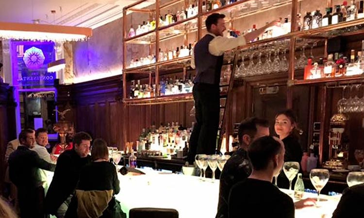 Some people drinking at the bar in The Continental, while bar staff serve drinks
