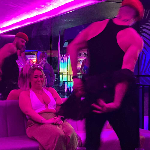 A male stripper taking his jacket off with a female member of our team wearing bunny ears who's sat watching in La Bamba bar 