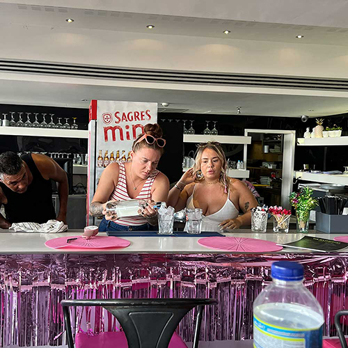 Two female members of our team making cocktails by pouring a bottle of spirits over ice 