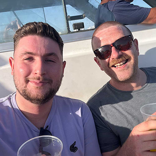  Two male members of our team posing for a photo on the boat with cups of beer in hand 