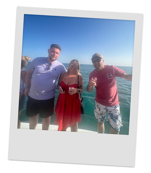 Three members of our team posing for a photo on the boat with their drinks and just the sea in the background