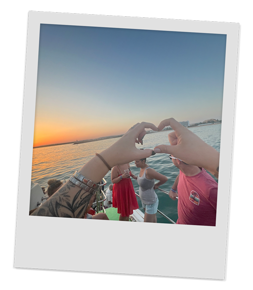 A member of our team making a love heart with their fingers with the boat party as a backdrop