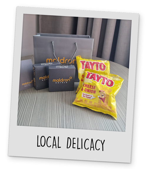 A giftbag with Maldron Hotels on it with two boxes of chocolates and two bags of Taytos crisps with the caption local delicacy