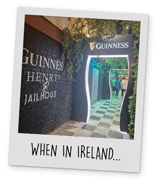 A magical looking alleyway with Guinness Henrys and the Jailhouse written on the wall and an archway that says Guinness with greenery draping down onto it