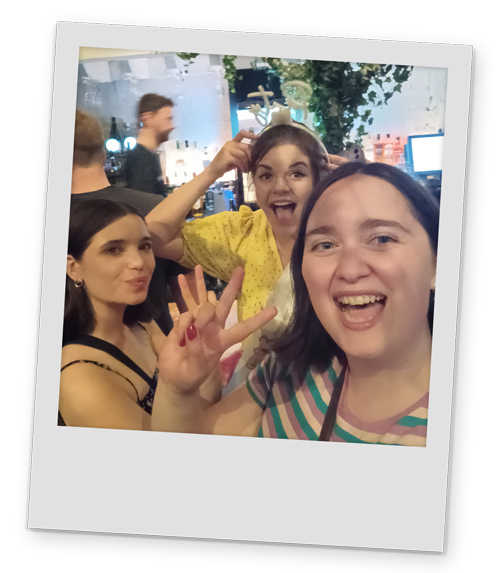 Three female members of the LNOF team doing peace signs for the camera with a bar in the background