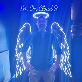  A male member of the LNOF team posing in front of a sign that says I'm on Cloud 9 at River Rooms. He has an outline of an angel behind him. 