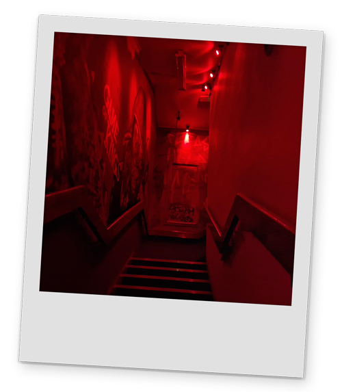 An eerie looking staircase with red lighting and graffiti on the walls