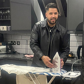 Akash in a kitchen ironing a shirt 