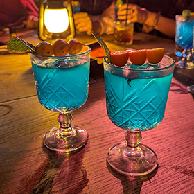 A round of bright blue cocktails with tiny oranges for garnish 