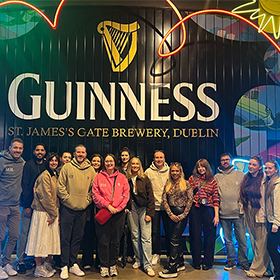  Team LNOF posing inside the Guinness Factory experience next to a big wall with lights and the words Guinness, St James's Gate Brewery Dublin 