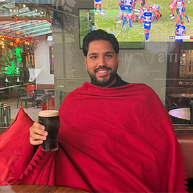 Akash sat in the Harcourt Hotel bar wrapped in a red blanket and posing with a Guinness 