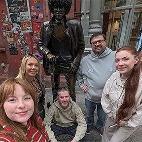  Five members of LNOF posing with a statue of a musician 