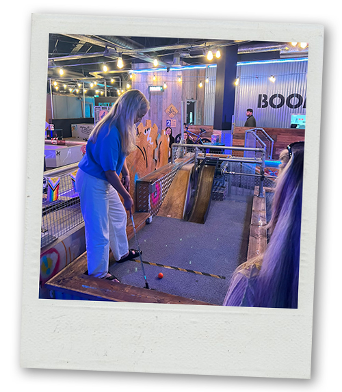 Katie about to hit a mini golf ball up a ramp as a part of Crazier Golf