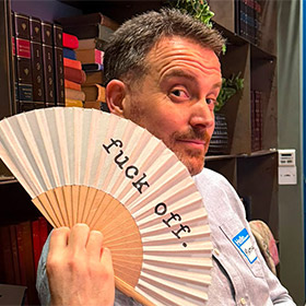  A male member of LNOF staff holding up a fan that reads Fuck off