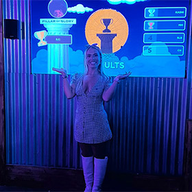  A female member of LNOF staff posing next to a darts board that reads Winner 