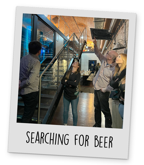 A polaroid style image of a group of people looking up in a Brewery in Krakow, with text reading 'Searching For Beer' at the bottom