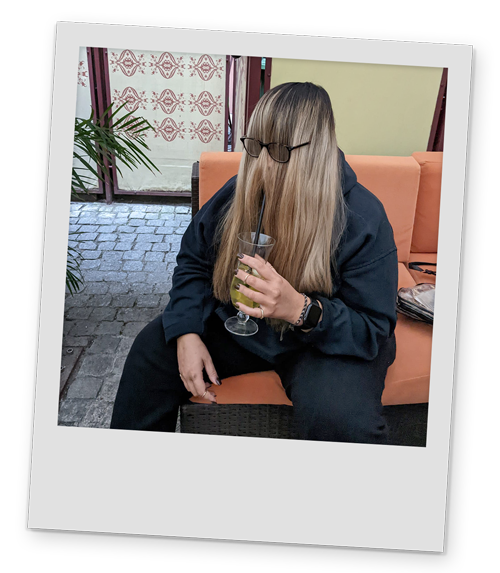 A polaroid style image of one of Team LNOF with their hair over their face, drinking a cocktail in Krakow
