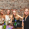  Four blonde women sat around a table with an exposed brickwork background. 