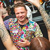 Lukas Tatek in a colourful shirt is smiling and the back of a woman's head holding her tattooed arms in the air. 