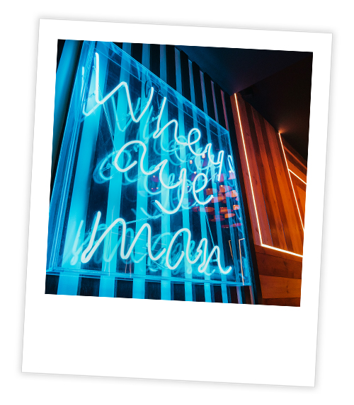 A Polaroid of a blue neon sign that reads Whey Aye Man