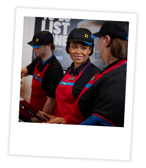 A Polaroid of three members of staff at Greggs who are stood at the till