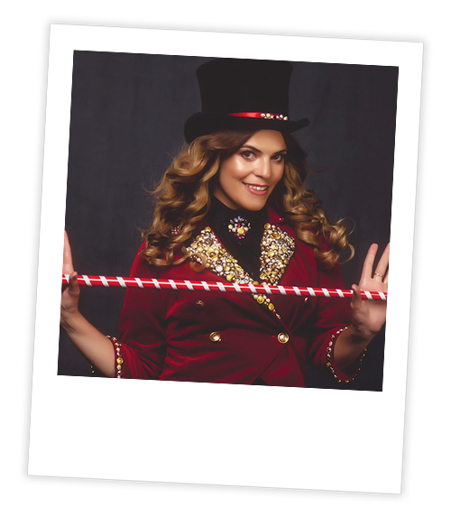 A Polaroid of a woman in a top hat and red jacket who is posing with a magic wand