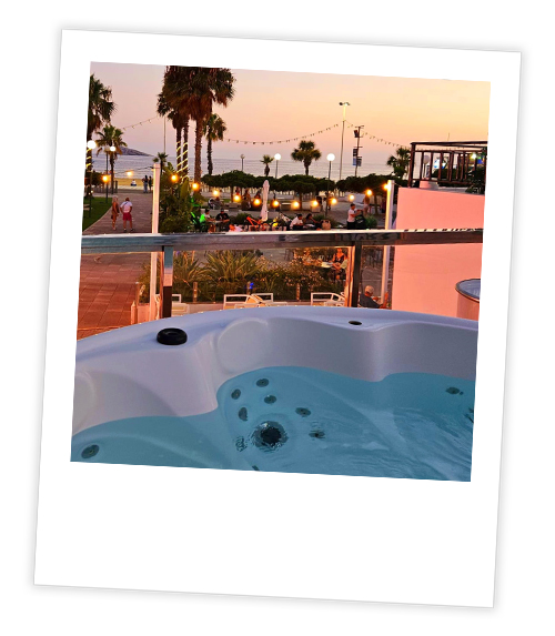 A Polaroid of a hot tub which is overlooking a beach club with the sun setting