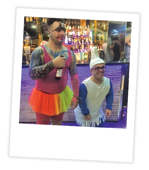 A Polaroid of a stag who has a tutu on who is handcuffed to a dwarf in a costume