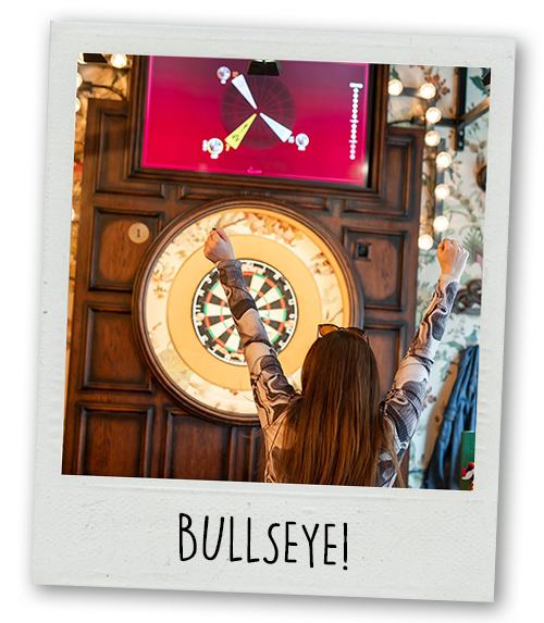 A Polaroid of a woman throwing a dart at a dart board with the caption Bullseye!